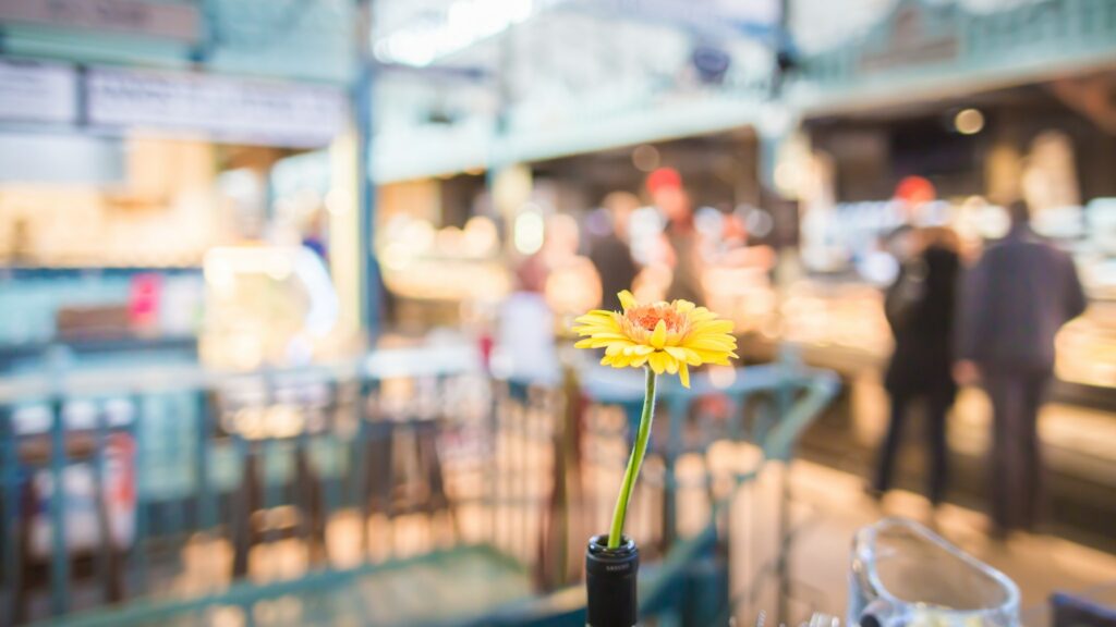 A yellow flower on a table and blurry Market Hall in the background